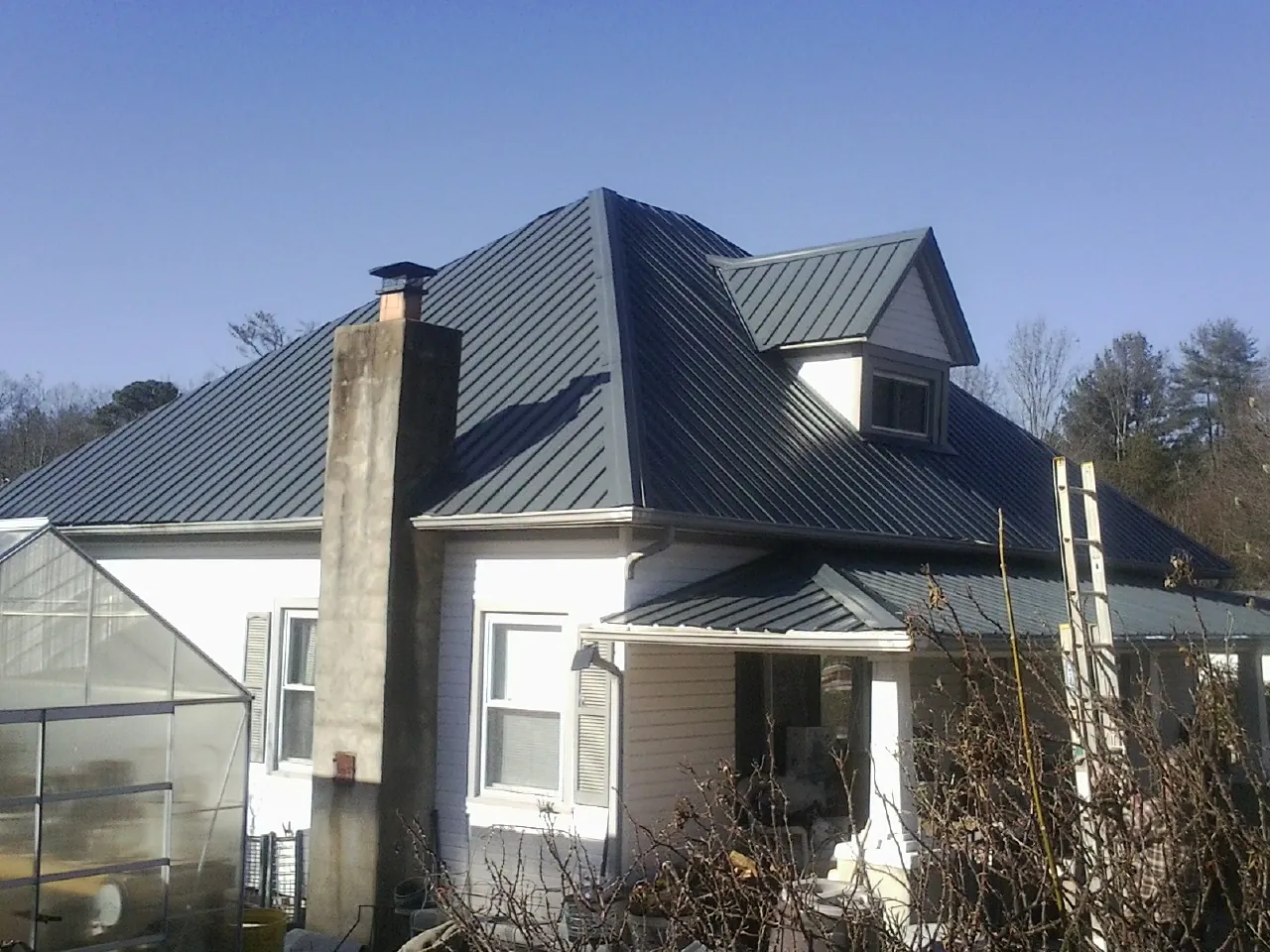 Dark blue standing seam metal roof on a white farmhouse with dormer — Slate & Tile Roof Repair by Roofing Brothers in Three Bridges