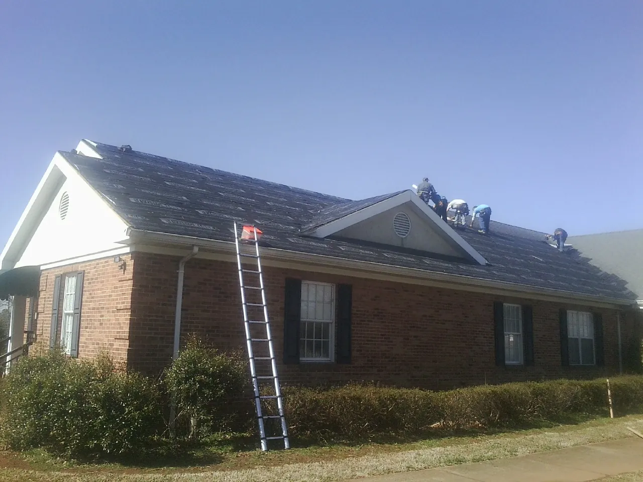 Crew tearing shingles off a brick ranch roof with a ladder set — Emergency Roof Repair work by our crew in Three Bridges