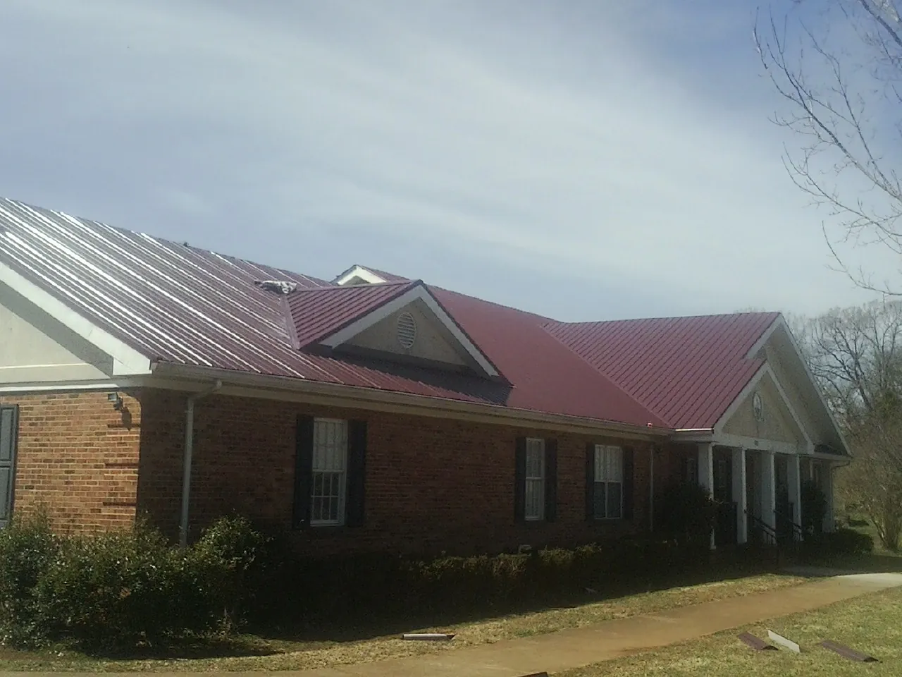 Red metal roof with gabled entries on a long brick building, from a Hail Damage Roof Repair job in Three Bridges