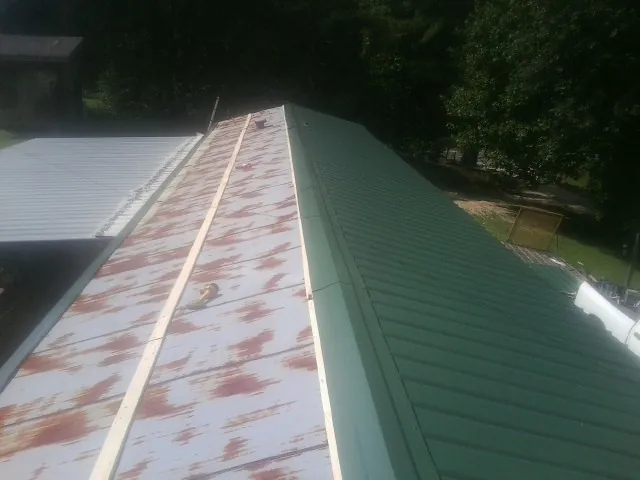 Old rusted panels beside newly installed green metal roofing — Wind Damage Roof Repair by Roofing Brothers in Three Bridges
