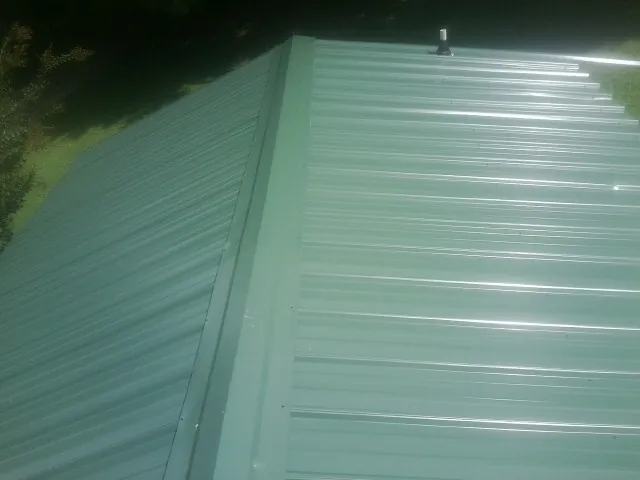 New green metal panels meeting at the ridge of a roof — Flat Roof Repair work by our crew in Three Bridges