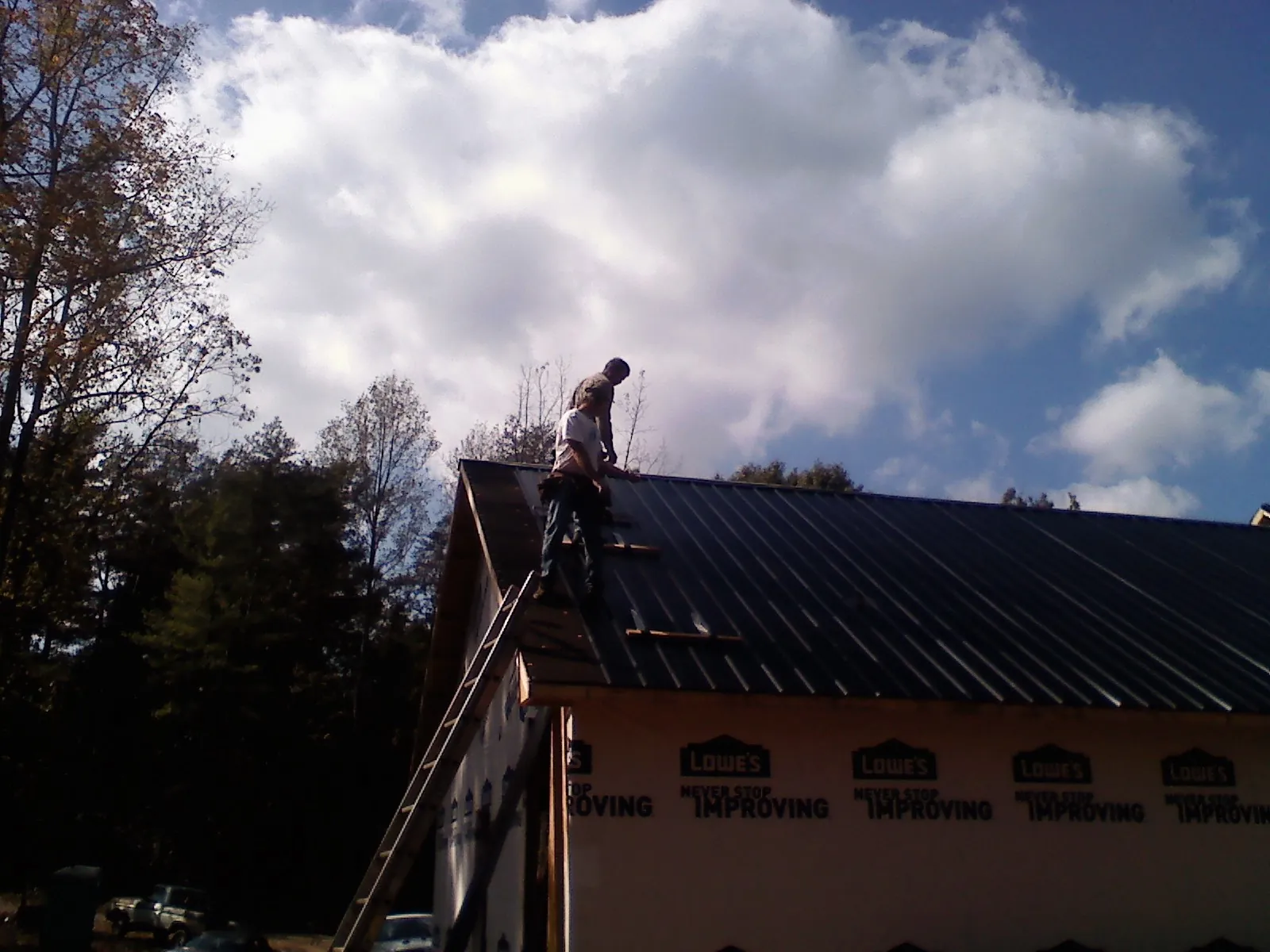 Roofer fastening dark metal panels high against a cloudy sky, from a Roof Inspection job in Three Bridges