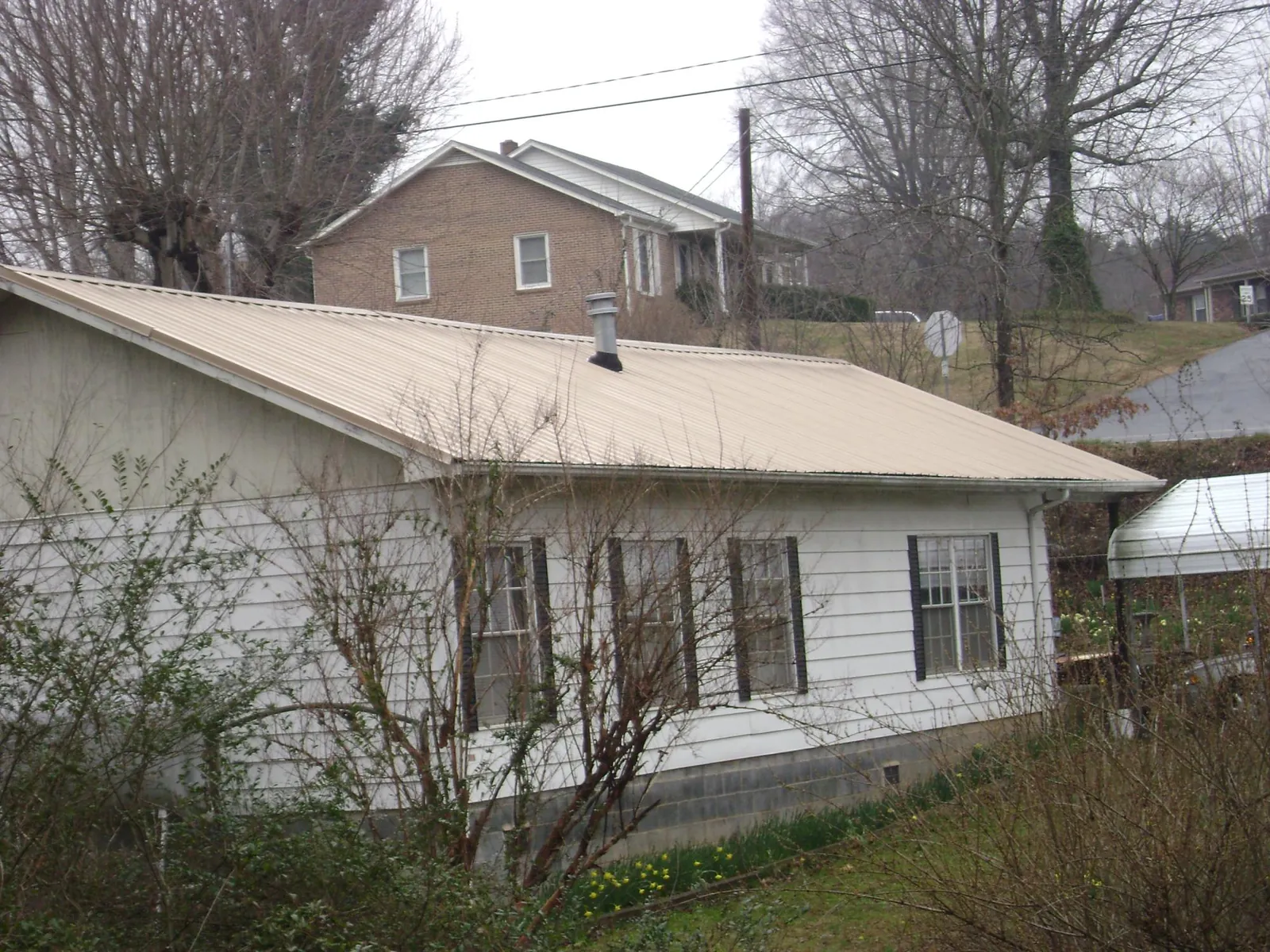 Tan metal roof on a white sided house set into a hillside — Commercial Roofing by Roofing Brothers in Three Bridges