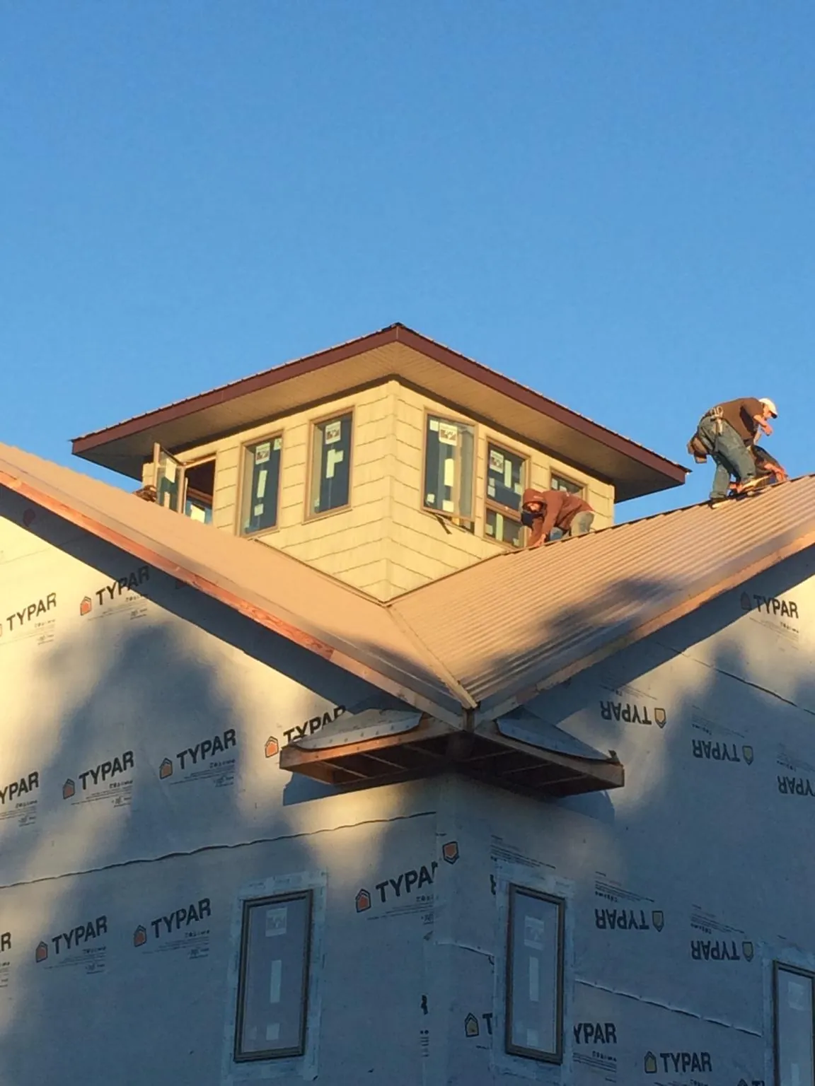 Roofers working around a rooftop cupola on a new metal roof at sunset — Roof Waterproofing in Three Bridges by Roofing Brothers